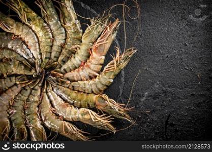 Fresh raw shrimp on a round stone board. On a black background. High quality photo. Fresh raw shrimp on a round stone board.