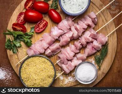 Fresh raw sliced turkey breast on skewer  with bulgur, with tomato sauce and herbs with salt on a cutting board on a wooden background top view close up