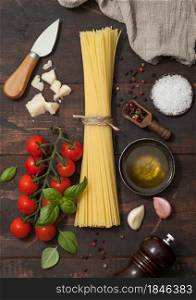 Fresh raw spaghetti pasta with cherry tomatoes and basil, garlic and oil with parmesan cheese and salt and pepper on wooden background.Top view