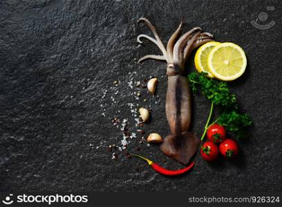 Fresh raw squid seafood herbs and spices with lemon tomato garlic on dark background