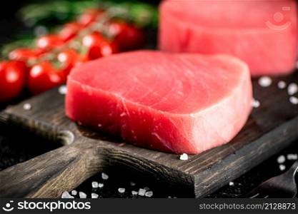 Fresh raw tuna on a cutting board with cherry tomatoes. Against a dark background. High quality photo. Fresh raw tuna on a cutting board with cherry tomatoes.
