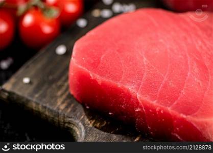 Fresh raw tuna on a cutting board with cherry tomatoes. Against a dark background. High quality photo. Fresh raw tuna on a cutting board with cherry tomatoes.
