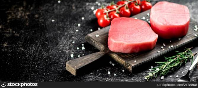 Fresh raw tuna on a cutting board with tomatoes, spices and rosemary. On a black background. High quality photo. Fresh raw tuna on a cutting board with tomatoes, spices and rosemary.