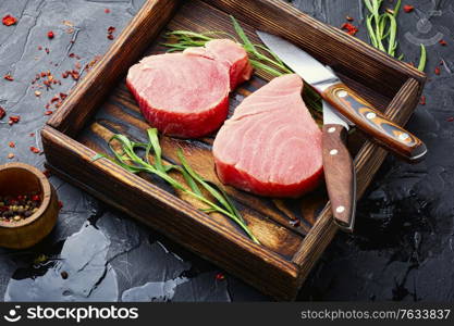 Fresh raw tuna steak and tarragon on kitchen table. Raw tuna fish