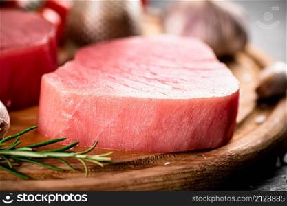 Fresh raw tuna steak with rosemary and garlic. On a rustic background. High quality photo. Fresh raw tuna steak with rosemary and garlic.