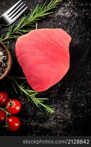 Fresh raw tuna steak with tomatoes and rosemary. On a black background. High quality photo. Fresh raw tuna steak with tomatoes and rosemary.