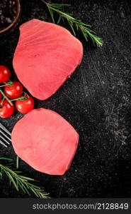 Fresh raw tuna steak with tomatoes and rosemary. On a black background. High quality photo. Fresh raw tuna steak with tomatoes and rosemary.