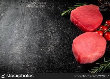 Fresh raw tuna steak with tomatoes and rosemary. On a black background. High quality photo. Fresh raw tuna steak with tomatoes and rosemary.