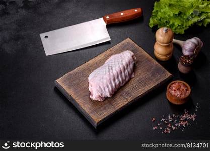 Fresh raw turkey wing with spices and herbs on a wooden cutting board against a dark concrete background. Preparation of ingredients for soup preparation. Fresh raw turkey wing with spices and herbs on a wooden cutting board