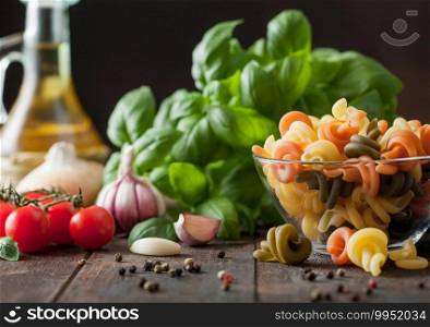 Fresh raw wheat trottole pasta in glass bowl with basil plant, oil and tomatoes with garlic and pepper on wooden table background.