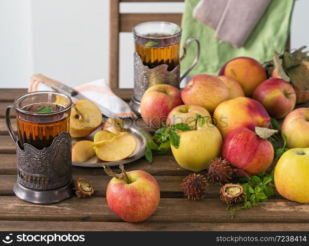 Fresh red apples and sliced apples on a wooden table. Wild grape leaves and mint leaves. Two glasses of mint tea. Autumn harvest. The fruits of the wild chestnut. Still life.