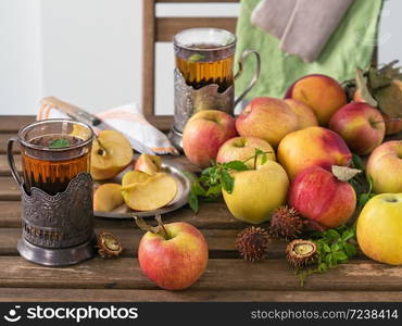 Fresh red apples and sliced apples on a wooden table. Wild grape leaves and mint leaves. Two glasses of mint tea. Autumn harvest. The fruits of the wild chestnut. Still life.