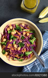 Fresh red cabbage, chickpea, carrot and broccoli salad in bowl with vinaigrette and lemon slices on the side, photographed overhead on slate with natural light. Red Cabbage, Chickpea, Carrot and Broccoli Salad