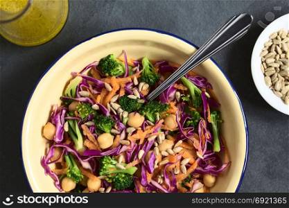 Fresh red cabbage, chickpea, carrot and broccoli salad with sunflower seeds in bowl with vinaigrette on the side, photographed overhead on slate with natural light (Selective Focus, Focus on the salad). Red Cabbage, Chickpea, Carrot and Broccoli Salad