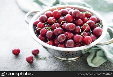 Fresh red cherries fruit in collander on a green textile background