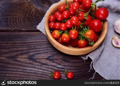 Fresh red cherry tomatoes in a wooden plate, empty space on the left