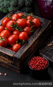 Fresh red cherry tomatoes in a wooden vintage box on a dark concrete background