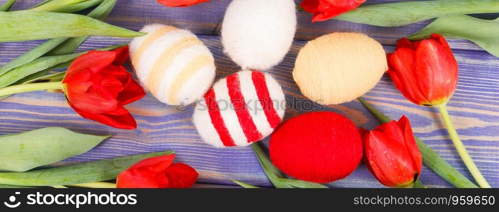 Fresh red tulips and eggs wrapped woolen string on boards as festive Easter decoration. Tulips and eggs wrapped woolen string on boards as festive Easter decoration