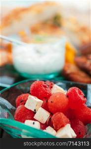 Fresh red watermelon and Feta cheese salad with sesame sauce close up image blurry dinner table background