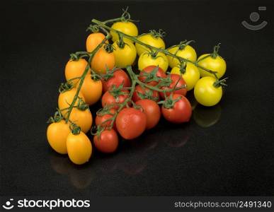 fresh red, yellow and orange cherry tomatoes on a black background with a reflection. wet tomatoes. tomatoes on a black background