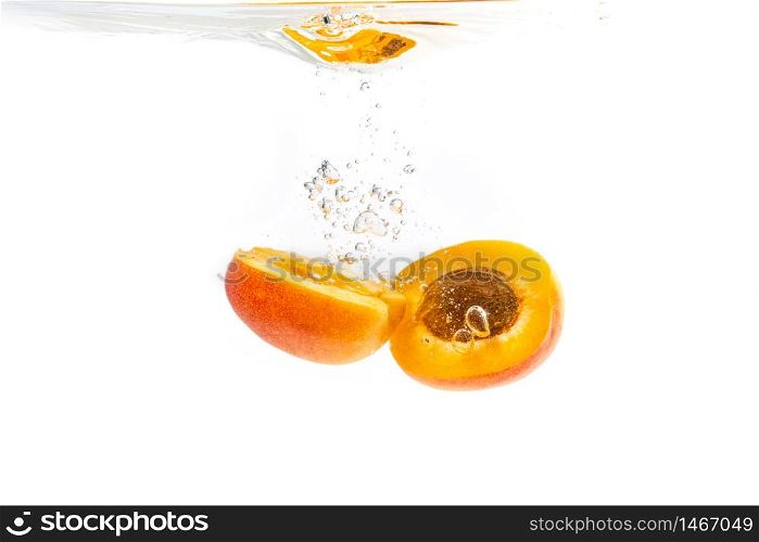 Fresh ripe apricot split in half falling in the clear water, isolated on white background. Fresh ripe apricot split in half falling in the clear water
