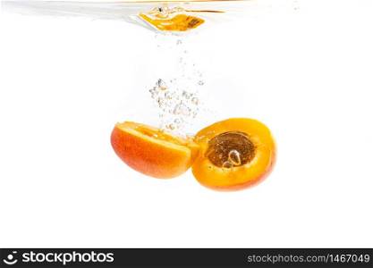 Fresh ripe apricot split in half falling in the clear water, isolated on white background. Fresh ripe apricot split in half falling in the clear water