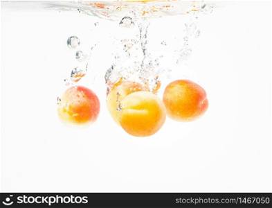 Fresh ripe apricots falling in the clear water, isolated on white background. Fresh ripe apricots falling in the clear water