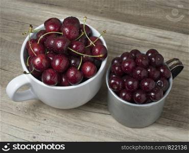 Fresh ripe cherries in cups, on wooden background. Top view.