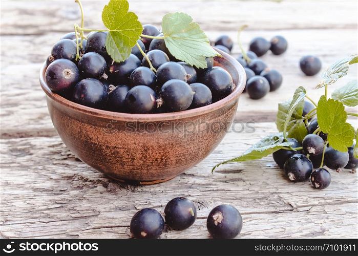 Fresh ripe currant berries in a bowl on a wooden background near green leaves. Juicy natural fruits currant. Black currant. Fresh ripe currant berries in a bowl on wooden background near green leaves. Juicy fruits currants. Black currant