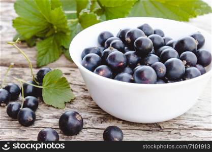 Fresh ripe currant berries in a white bowl on wooden background near green leaves. Juicy natural fruits currant. Black currant. Fresh ripe currant berries in a white bowl on wooden background near green leaves. Juicy fruits currant. Black currant