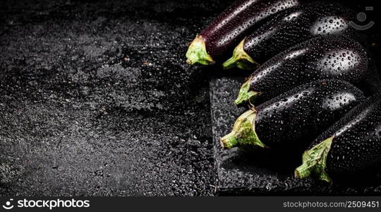 Fresh ripe eggplant with droplets of water on a stone board. On a black background. High quality photo. Fresh ripe eggplant with droplets of water on a stone board. 
