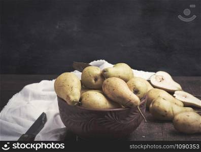 fresh ripe green pears in a brown clay bowl on a table, close up