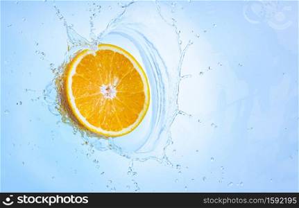 Fresh ripe half of orange splashing into clear water, isolated on light blue background. Health food concept. Fresh ripe half of orange fruit splashing into clear water.