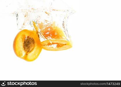 Fresh ripe organic apricot split in half falling in the clear water, isolated on white background. Fresh ripe peach split in half falling in the clear water