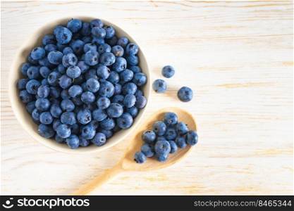 Fresh ripe organic blueberries in bowl and wooden spoon with berries on white wooden background. Flat lay, top view with copy space for text. Fresh ripe organic blueberries in bowl on white wooden background