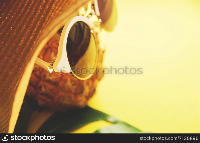 Fresh ripe pineapple with sunglasses in hat and a leaf of monstera tree on color background, top view