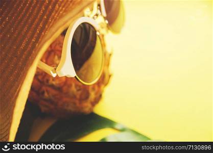 Fresh ripe pineapple with sunglasses in hat and a leaf of monstera tree on color background, top view