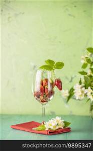 Fresh ripe raw strawberry with green leaves in the wine glass on green surface.