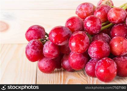 Fresh ripe red grapes are placed on a wooden floor.