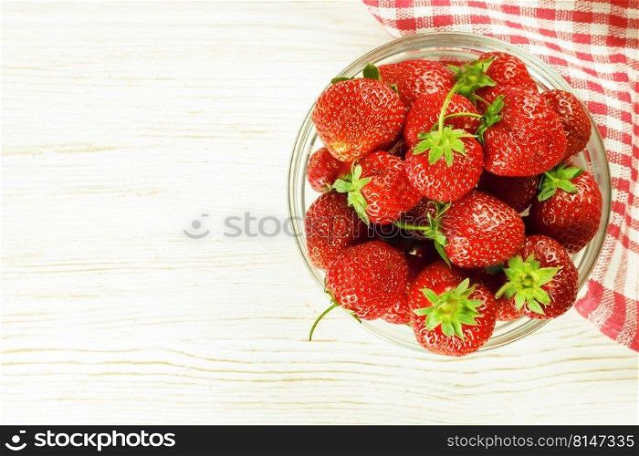 Fresh ripe red strawberry in a bowl on a white wooden table. Top view, flat lay, mockup with copy space for text. Strawberry in a bowl on white wooden background