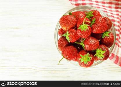 Fresh ripe red strawberry in a bowl on a white wooden table. Top view, flat lay, mockup with copy space for text. Strawberry in a bowl on white wooden background