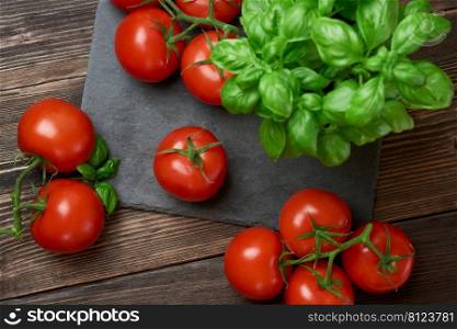 Fresh ripe red tomatoes on a cutting board with fresh basil on a wooden background. Freshly picked red tomatoes and basil leaves for cooking. top view 