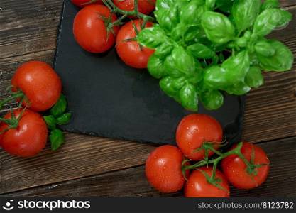 Fresh ripe red tomatoes on a cutting board with fresh basil on a wooden background. Freshly picked red tomatoes and basil  leaves for cooking. top view 