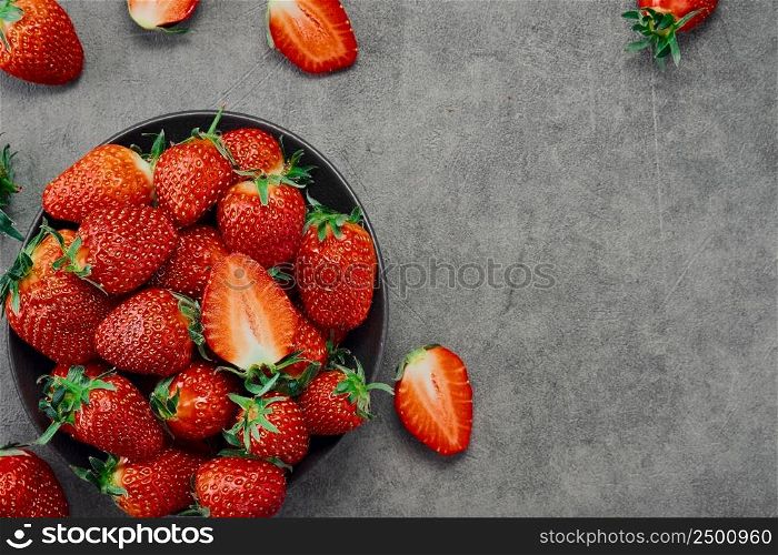 Fresh ripe strawberries and half a berry in a plate on a gray table, top view with copy space. Seasonal juicy berry