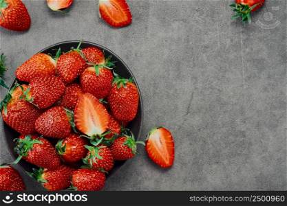Fresh ripe strawberries and half a berry in a plate on a gray table, top view with copy space. Seasonal juicy berry