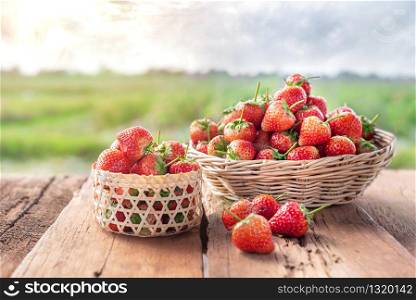 fresh ripe strawberries in basket over wooden floor with green field background. fresh ripe strawberries in basket