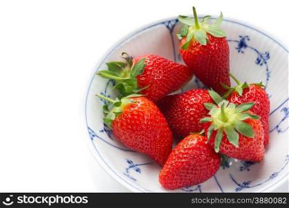 Fresh ripe strawberries, source of antioxidants and vitamin C, in a white bowl with blue decorative pattern, to be served as a healthy snack or dessert, high-angle close-up with copy space on white