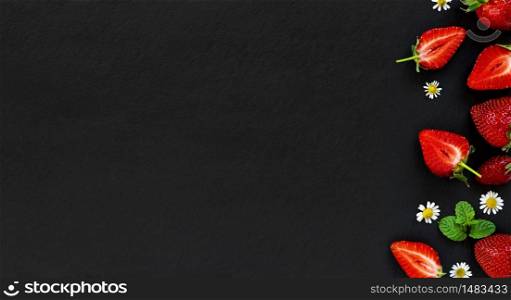 Fresh, ripe strawberries, whole and cut to the right on a black stone background, with copy space for text. Top view.