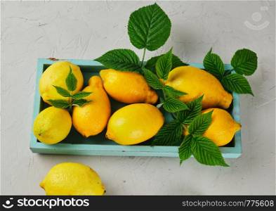 fresh ripe whole yellow lemons on a blue wooden board, ingredients for making summer drinks, top view