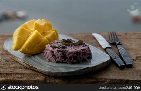Fresh ripe yellow mango fruit (Barracuda mango) and Riceberry topping pandan leaf on ceramic plate served with knife and fork. Selective focus.